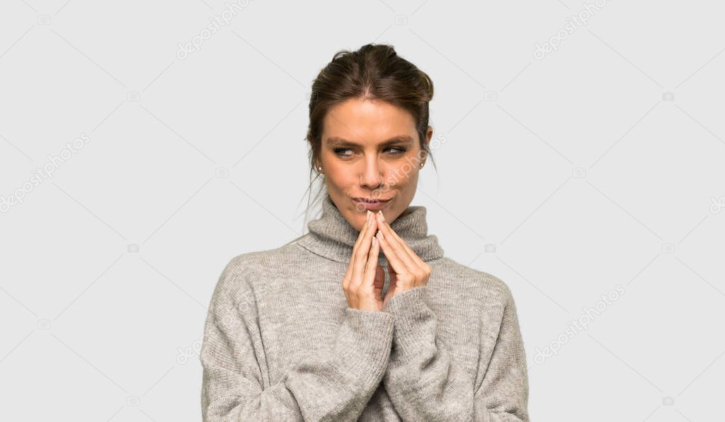 Blonde woman with turtleneck scheming something over isolated grey background