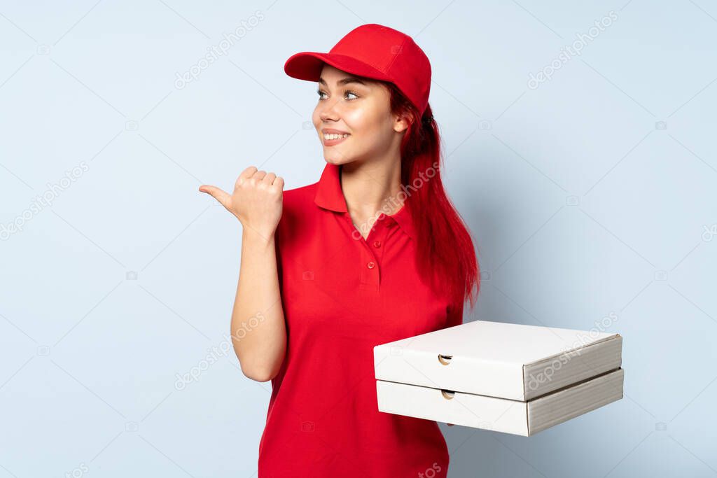 Pizza delivery girl holding a pizza over isolated background pointing to the side to present a product