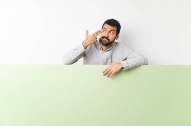 Sakallı genç yakışıklı adam elinde kocaman yeşil boş bir afiş tutarken intihar jesti yapmada sorun yaşıyor.