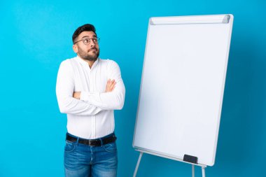 Beyaz tahtada bir sunum yapan iş adamı beyaz tahtada bir sunum yapıyor ve şüphe jesti yapıyor.