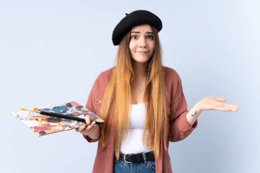 Mavi arka planda izole edilmiş bir palet tutan genç bir sanatçı kadının kafası karışmış yüz ifadesi ile ilgili şüpheleri var.