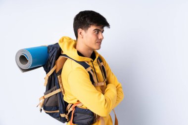 Genç dağcı büyük bir sırt çantası ile izole edilmiş mavi arka plan gülüyor.