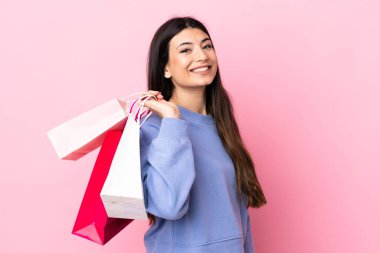 Soyutlanmış pembe arka planda genç esmer kız alışveriş torbaları tutuyor ve gülümsüyor.