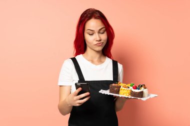 Pasta şefi elinde bir kek tutuyor. Pembe arka planda izole edilmiş. Düşünüyor ve mesaj gönderiyor.