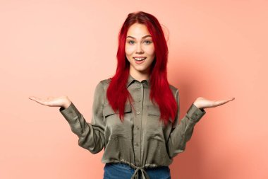 Genç kızıl saçlı kız pembe arka planda izole edilmiş ve şok olmuş bir yüz ifadesi var.