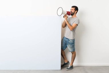 Sakallı genç yakışıklı adam elinde kocaman mavi bir levhayla megafondan bağırıyor.