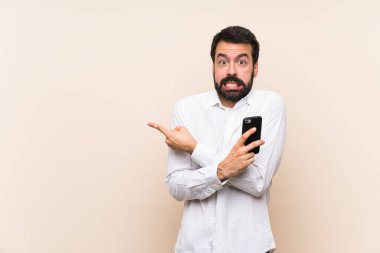 Sakallı genç adam elinde bir cep telefonu var. Korkmuş ve yan tarafı işaret ediyor.