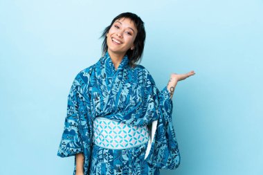 İzole edilmiş mavi arka planda kimono giyen genç bir kadın bir ilan vermek için avucunda hayali bir fotokopi makinesi tutuyor.