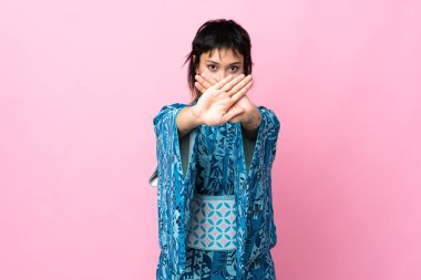 İzole edilmiş mavi arka planda kimono giyen genç bir kadın bir eylemi durdurmak için eliyle jest yapıyor.