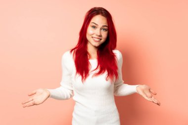 Genç kızıl saçlı kız pembe arka planda izole edilmiş mutlu ve gülümsüyor.