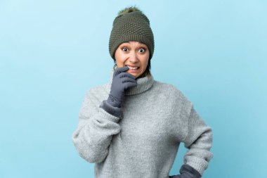 Kış şapkalı genç Uruguaylı kız mavi arka planda izole edilmiş gergin ve korkmuş.