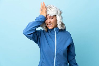 Mavi arka planda izole edilmiş, kış şapkalı genç Uruguaylı kız, kafa karıştırıcı yüz ifadesi ile ilgili şüpheleri var.