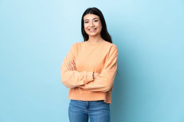 Genç esmer kız izole edilmiş mavi arka planda kollarını ön cephede çapraz tutuyor.