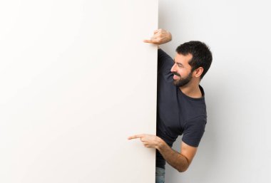 Sakallı, kocaman boş bir pankart tutan yakışıklı bir genç.