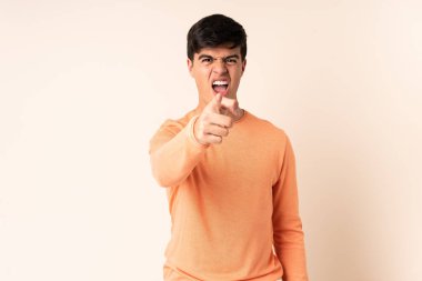 İzole edilmiş bej arka planda yakışıklı bir adam hayal kırıklığına uğramış ve ön tarafı işaret ediyor.