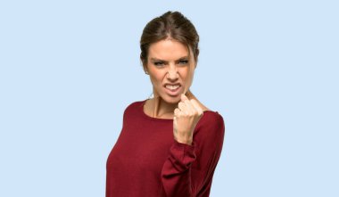 İzole edilmiş mavi arka planda kızgın jestli sarışın kadın.