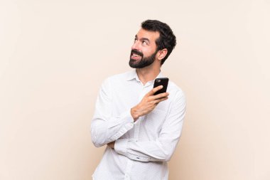 Sakallı genç adam gülümserken yukarı bakıyor.