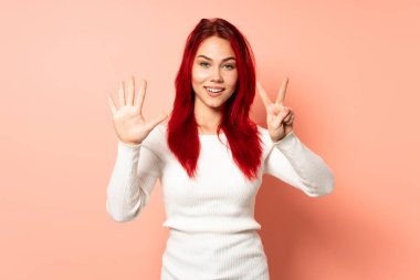 Pembe arka planda izole edilmiş genç kızıl saçlı kız yediyi parmaklarıyla sayıyor