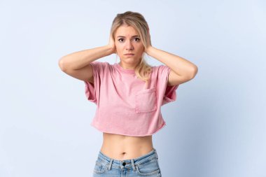 Sarışın kadın izole edilmiş mavi arka planda hayal kırıklığına uğramış ve kulaklarını kapatmış.