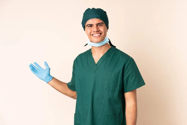 身穿蓝色制服的外科医生站在孤立的背景上 手心上还带着想象中的复制空间 — 图库照片