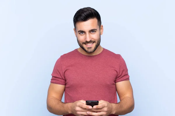 Mavi Arka Planda Sakallı Yakışıklı Genç Adam Cep Telefonuyla Mesaj — Stok fotoğraf