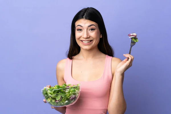 Young woman with salad over isolated purple background