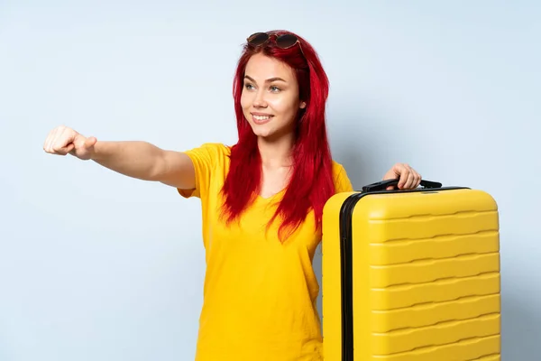 带着一个蓝色背景的手提箱的旅行女孩举起一个大拇指 — 图库照片