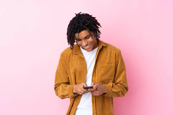 身穿灯芯绒夹克 背景为粉色的年轻非洲裔美国人用手机传达了一个信息 — 图库照片