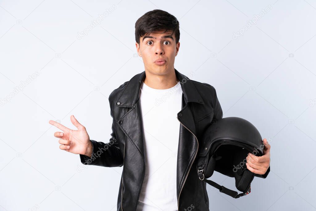 Man with a motorcycle helmet over isolated blue background pointing to the laterals having doubts
