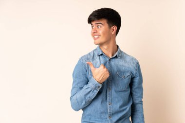 İzole edilmiş bej arkaplan üzerinde yakışıklı bir adam bir ürün sunmak için kenarı işaret ediyor