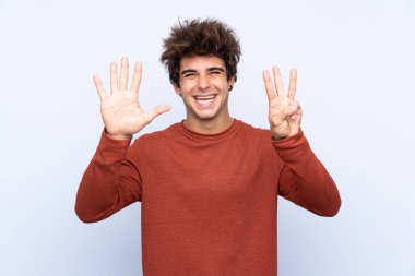 İzole edilmiş mavi arka planda genç beyaz adam parmaklarıyla sekizi sayıyor.