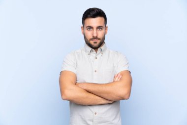 Sakallı, mavi arka planda genç yakışıklı adam kollarını kavuşturuyor.