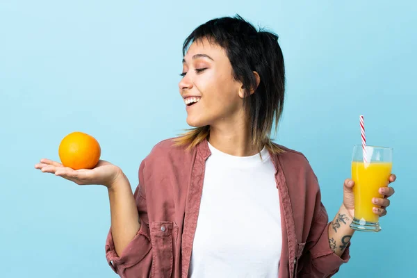 Joven Uruguaya Sobre Fondo Azul Aislado Sosteniendo Una Naranja Zumo — Foto de Stock