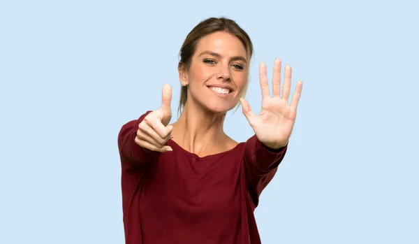 Blonde woman counting six with fingers over isolated blue background