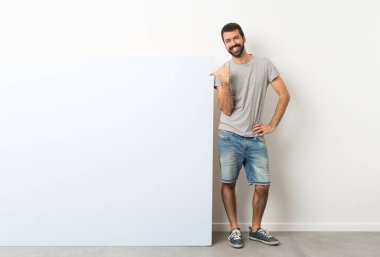 Sakallı genç, yakışıklı bir adam. Elinde kocaman mavi bir pankart var. Yan tarafı göstererek bir ürün sunuyor.