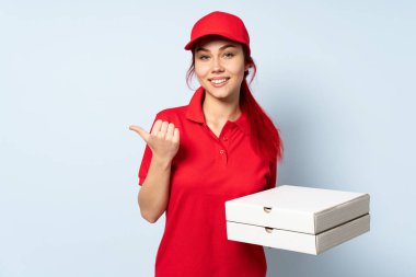 Pizza teslimatçısı kız izole edilmiş arka planda pizza tutuyor. Başparmakları havada ve gülümsüyor.