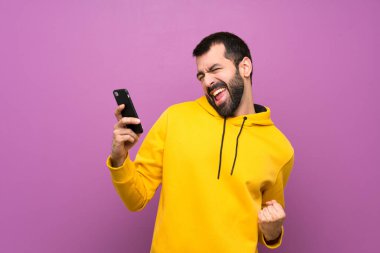 Sarı svetşörtlü yakışıklı ve telefonu zafer pozisyonunda.