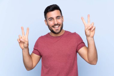 Mavi arka planda sakallı yakışıklı genç adam iki eliyle zafer işareti gösteriyor.