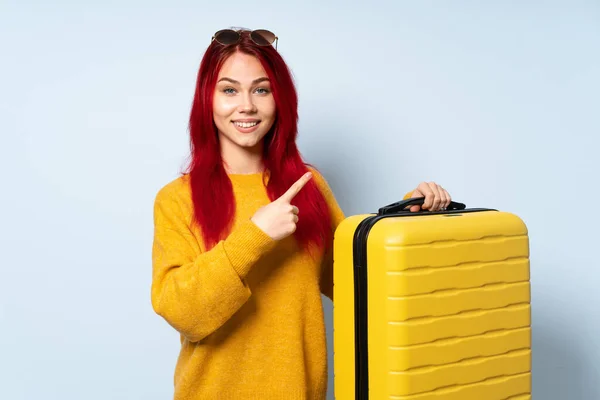 一个旅行女孩拿着一个蓝色背景的手提箱 指着旁边展示一个产品 — 图库照片