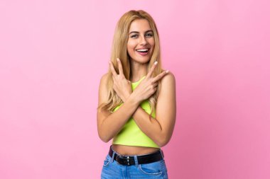 Genç Uruguaylı sarışın kadın izole pembe arka planda gülümsüyor ve zafer işareti gösteriyor.