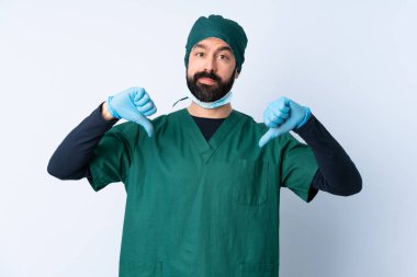 Yeşil üniformalı bir cerrah, izole edilmiş arka planda baş parmağını iki eliyle gösteriyor.