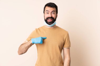 Koronavirüsten sakallı beyaz bir adam maske ve eldivenlerle korunuyor.