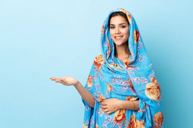 Geleneksel kostümlü genç Faslı kadın mavi arka planda izole edilmiş bir fikir sunuyor.