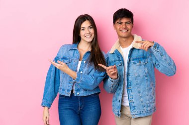 Soyutlanmış pembe arka planda genç bir çift sessizlik işareti gösteriyor. Parmağını ağzına sokuyor.