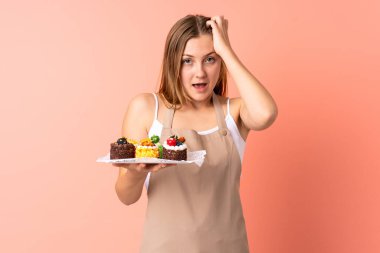 Ukraynalı aşçı pembe arka planda yüzünde sürpriz bir ifadeyle izole edilmiş bir kek tutuyor.