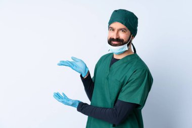 Yeşil üniformalı cerrah, izole edilmiş arka planda. Davet etmek için ellerini yana uzatıyor.