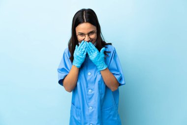 Cerrah kadın mavi arka planda mutlu ve gülümsüyor elleriyle ağzını kapatıyor.
