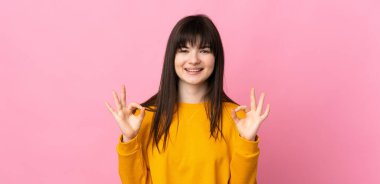 Pembe arka planda izole edilmiş genç Ukraynalı kadın iki eliyle tamam işareti gösteriyor.