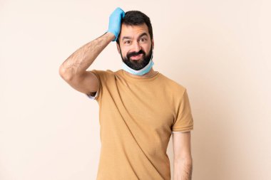 Koronavirüsten sakallı beyaz bir adam maske ve eldivenle korunuyor. Arkaplanda soyutlanmış bir geçmiş var. Hayal kırıklığı ifadesi var.