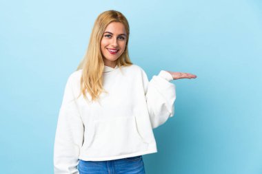 Genç Uruguaylı sarışın kadın, izole edilmiş mavi arkaplanda bir ilan vermek için fotokopi makinesi tutuyor.